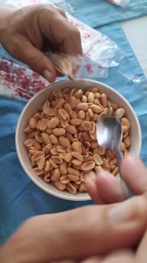 Adamın biri bir kaseden fıstık toplamak için kaşık kullanıyor ve sonra onları plastik bir torbaya koyuyor. Bireysel tüketim için paketlenmiş