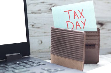 Cüzdanın içinde vergi günü notu, dizüstü bilgisayarın yanında, vergi ödeme konsepti.