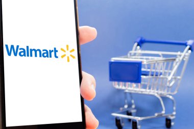 Bogota, Kolombiya - 24 Şubat 2025: Telefon ekranında Walmart logosu yanında mavi arka planda minyatür market arabası. Amerika 'nın en büyük çevrimiçi alışveriş zincirlerinden biri..