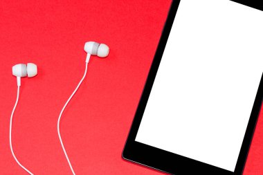 Boş ekranlı tablet ve kırmızı arka planda kulaklık, sesli kitapların dünyasını vurguluyor. Çevrimiçi multimedya tüketimi