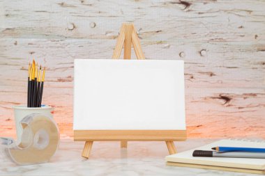 Resim sehpasında boş tuval, kalemler, bant ve defter ile düzenlenmiş sanatsal alan. Sanat stüdyosu. Yaratıcı projelerin oluşturulması