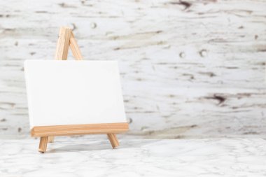 Ahşap bir arka planda, ahşap bir sehpanın üzerinde küçük boş bir tuval, evde resim yapmak için uygun sıcak bir atmosfer. Kopyalama alanı kullan
