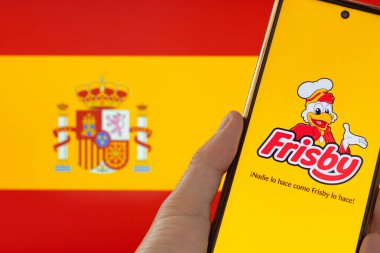 Bogota, Kolombiya - 14 Mayıs 2025. Frisby logosunu gösteren cep telefonu İspanya bayrağının arka planında kızarmış tavuk restoranı, ismin o ülkeye kaydedilmesi konusundaki tartışmalara atıfta bulunuyor.