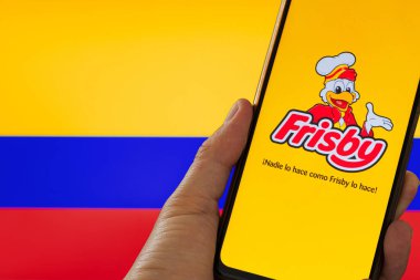 Bogota, Kolombiya - 14 Mayıs 2025. Frisby uygulaması ev yapımı cep telefonu Kolombiya bayrağı önünde bir el tarafından tutuluyor. Yasal bir tartışmanın ortasında ulusal kimliğin sembolü. Kolombiya restoran zinciri için sosyal medya desteği