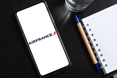 Bogota, Kolombiya - 13 Mayıs 2025: Fransa Hava Yolları 'nı gösteren cep telefonu, bir bardak su ve kalemle defter yanındaki karanlık masada.