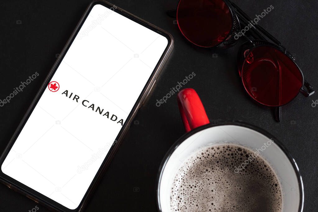 Bogota, Colombia - May 13, 2025: Air Canada logo on cell phone screen between coffee cup and sunglasses on elegant black textured background. Travel concept