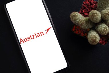 Bogota, Kolombiya - 13 Mayıs 2025: Avusturya Havayolları logosu olan cep telefonu zarif koyu arkaplan üzerine dekoratif kaktüs bitkisinin yanında