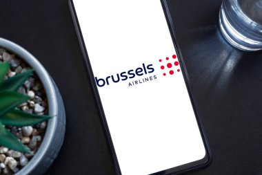 Bogota, Kolombiya - 13 Mayıs 2025: Brüksel Havayolları, Belçika 'dan bir havayolu şirketi, karanlık bir yüzey üzerinde sulu bir bitki ve bir bardak su bulunan bir cep telefonuyla