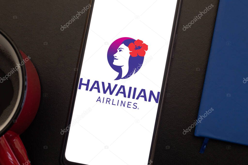 Bogota, Colombia - May 13, 2025: Cell phone display with Hawaiian Airlines, airline from the United States, next to a book and a cup of coffee, tropical concept and leisure travel from the island