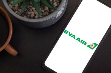 Bogota, Kolombiya - 13 Mayıs 2025: EVA Air, Tayvan Havayolları, cep telefonu ekranında beyaz arka planda, sulu ve modern ortamda kahve fincanının yanında
