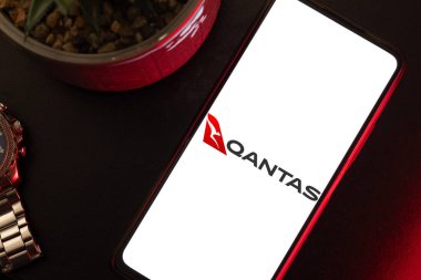 Bogota, Kolombiya - 13 Mayıs 2025: Qantas, Avustralya ulusal havayolu, cep telefonuyla bir saatin yanında, kıtalararası seyahat sahnesi ve Avustralyalı gezgin yaşam tarzı