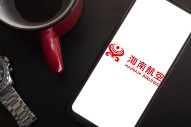 Bogota, Kolombiya - 13 Mayıs 2025: Hainan Havayolları logosu, Çin havayolları, masasında kırmızı bardak ve saat, Asya turizmi ve küresel hareketliliğe odaklı şirket imajı