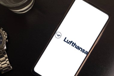 Bogota, Kolombiya - 13 Mayıs 2025: Lufthansa, Almanya 'nın önde gelen havayolu şirketi, cep telefonu ekranında, bir bardak su ve saatle karanlık arka planda, Avrupa iş estetiği ve hava zarafeti