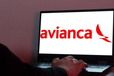 Bogota, Kolombiya - 14 Mayıs 2025: Kolombiya 'nın en önemli havayolu şirketi Avianca logosu ile dizüstü bilgisayar, kırmızı ışık ile karanlık masa üzerinde, el ile internetten uçuş rezervasyonu sırasında etkileşim içinde