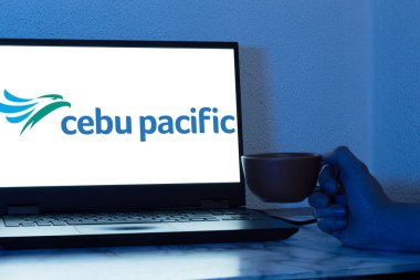 Bogota, Kolombiya - 14 Mayıs 2025: Cebu Pacific 'in logosu, dizüstü bilgisayarı ve kahve fincanı ile ön planda tutulan