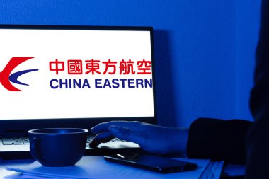 Bogota, Kolombiya - 14 Mayıs 2025: Çin Doğu Havayolları 'nın logosunu gösteren dizüstü bilgisayar ekranı, Çin anakarası havayolu, kahve fincanı, evrak ve cep telefonu masası, uluslararası uçuş rezervasyonu için rahat bir sahne