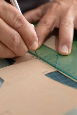 Saydam bir cetvel ve bir kesiciyle bir adamın ellerinin kartondan kesme çizgileri yakın plan.