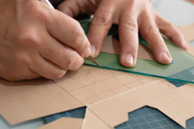 Cetvel ve metal neşterle karton katları işaretleyip kesen eller.