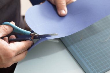 Çalışma masasında makasla mavi bir kart dilimini kesiyorsun.