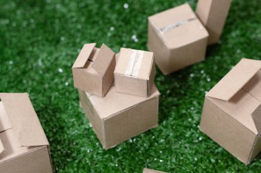 Yapay çimlerin üzerine istiflenmiş küçük karton kutular, teslimat, dağıtım ve çevrimiçi ticaret öneren mini mini paketler.