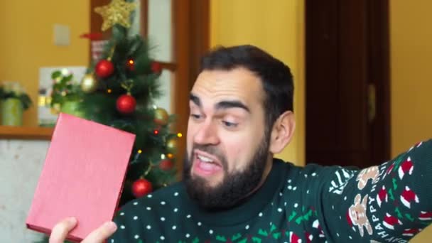 一个快乐的大胡子男人的自拍兴奋地在圣诞树前收到包装好的礼物 身穿圣诞毛衣 — 图库视频影像