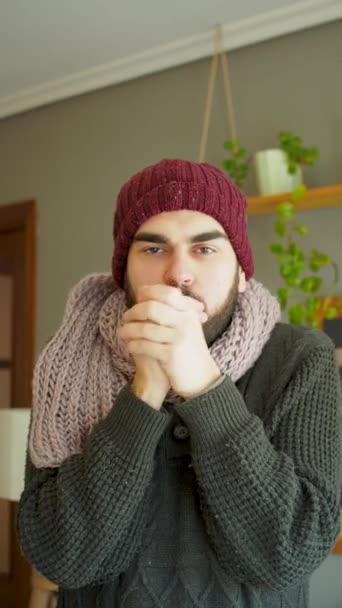 若いひげを生やした男が冷たい波と戦うために毛布で身を覆っていた 居心地の良いリビングルームで冬服を着て Uhd垂直ビデオ — ストック動画
