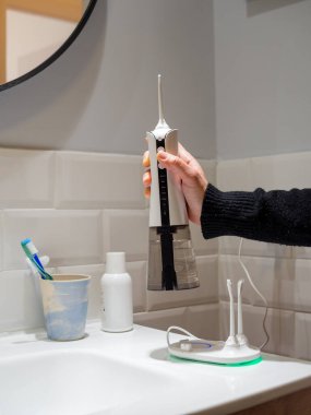 young woman holding a domestic wireless dental water flosser on the bathroom wash basin