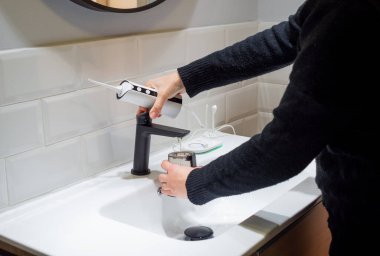  Effortless Oral Health: Woman Filling Water Flosser Tank at Bathroom Basin