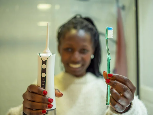 Maintaining a healthy smile: a young woman performs her dental hygiene routine at home using a domestic dental water flosser and her dental toothbrush.