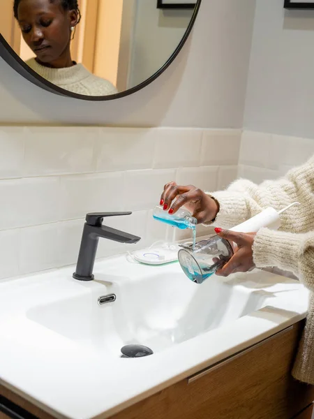 Effortless Oral Health: Woman Filling Water Flosser Tank with Mouthwash at Bathroom Basin