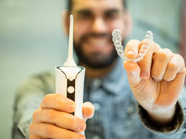 Maintaining a healthy smile: a young man performs her dental hygiene routine at home using a domestic dental water flosser and his dental aligner.