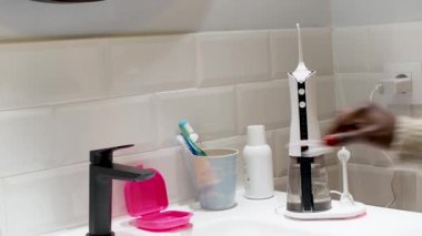 young woman keeping her dental aligner taking and placing a domestic wireless dental water flosser on the bathroom wash basin