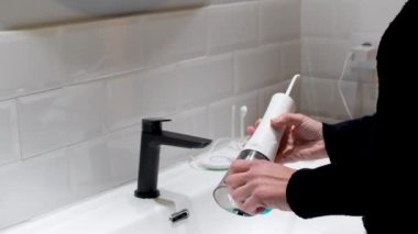 Effortless Oral Health: Woman Filling Water Flosser Tank at Bathroom Basin