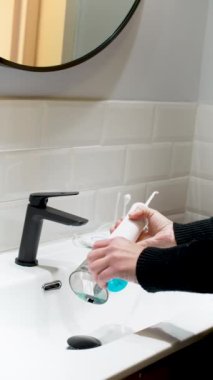  Effortless Oral Health: Woman Filling Water Flosser Tank at Bathroom Basin 4K vertical video