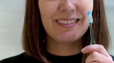 Sağlıklı bir gülümseme takınıyor: genç bir kadın diş hijyen rutinini evde diş fırçası ve diş fırçası kullanarak gerçekleştiriyor.