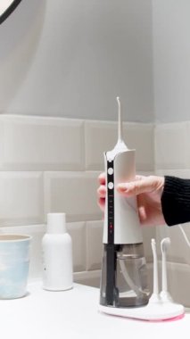 Genç bir kadın, banyo yıkama leğenine 4K dikey video kablosuz diş ipi alıp yerleştiriyor.