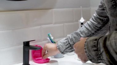Delikanlı diş hizasını koruyor. Tuvaletteki lavaboya kablosuz diş ipi kullanıyor.