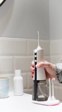 young man keeping his dental aligner taking a domestic wireless dental water flosser on the bathroom wash basin 4K Vertical video