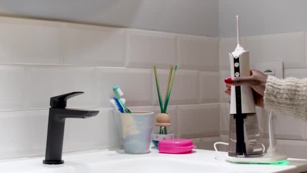 若い女性が浴室の洗面台に国内の無線歯科用水洗器を設置し — ストック動画