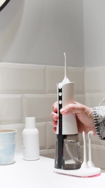 浴室の洗面台で国内の無線歯科用水の花を取る彼の歯のアライナーを保つ若い男4K垂直ビデオ — ストック動画