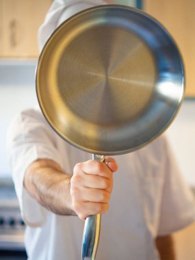 Portrait of a chef hiding his face with a stainless pan