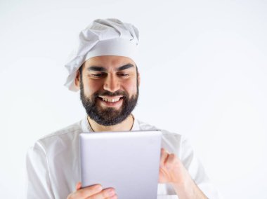 Genç aşçı bir tablet kullanıyor, yemek tarifi okuyor. Beyaz bir arkaplanda izole edilmiş