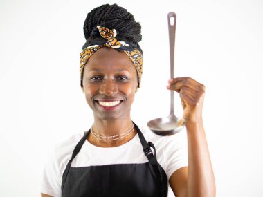 Genç bayan şef gülümseyip kameraya bakarken metal kepçe gösteriyor. Beyaz bir arkaplanda izole edilmiş