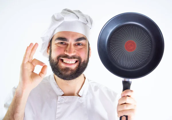 年轻的男性厨师一边微笑着一边看着相机 展示着一个不粘的锅子 被白色背景隔离 — 图库照片