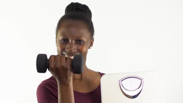体重計を見せる若い女性と白い背景に隔離されたダンベルを持ち上げる — ストック動画