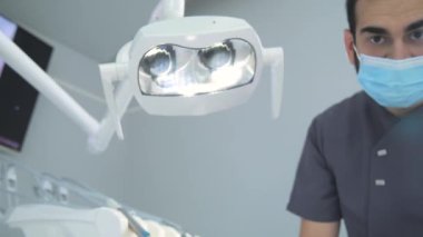 Klinikte muayene sırasında maske ve eldiven takan genç bir dişçi.