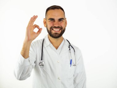 Genç erkek doktor gülümserken imza atın. Beyaz arkaplanda izole edilmiş kameraya bak