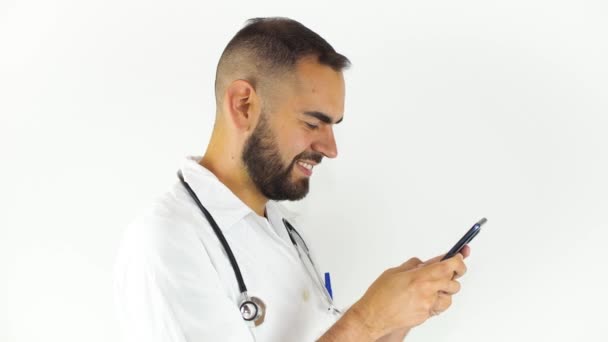 スマートフォンで微笑んでいる若い男性医師 白い背景に隔離される — ストック動画