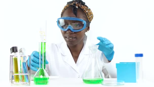 測定シリンダーからビーカーに液体サンプルを注ぐ実験室で保護眼鏡をかけた若い女性科学者 — ストック動画