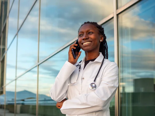 young female doctor talking by phone outdoors in front of a hospital
